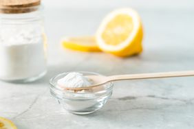 Jar with baking soda, lemon and wooden spoon on marble table background.